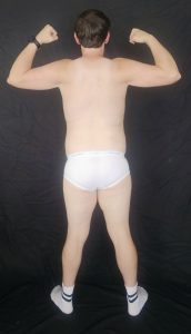 Joshua Marron facing backward, flexing both arms in white briefs and socks for Project Legacy muscle progress photo.