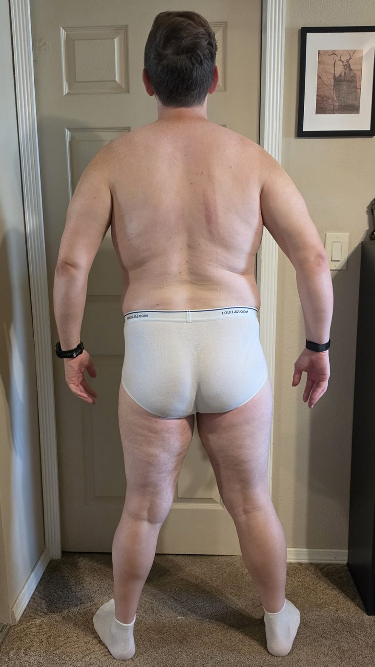 Week 1 progress photo of Joshua Marron in white briefs and socks, standing in a Back pose for the Resurgam transformation.